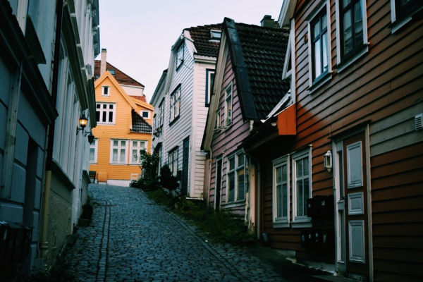 A cobblestone street lined with colorful, wooden houses, with a prominent yellow house at the end. The street incline steeply up toward the yellow house. 