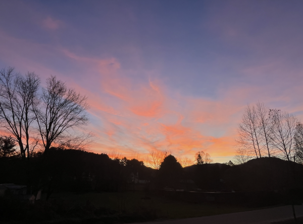 another view of a darkening blue sky and a dark mountained horizon and lots of pink and light red clouds in a sunset