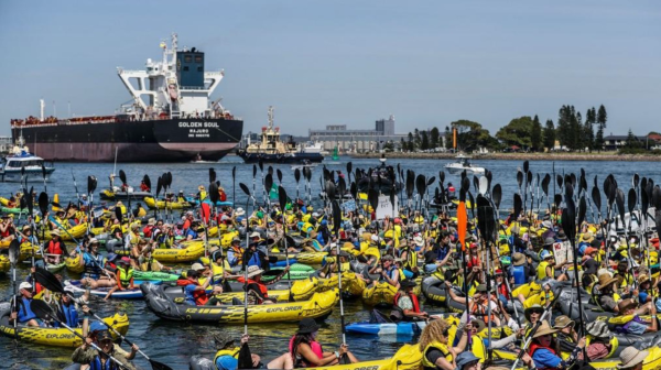 Mass of protesters on kayaks in Newcastle river with coal ship in background preparing to block the next one