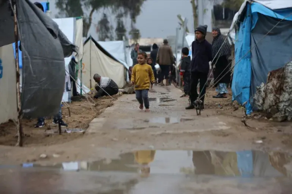 A child runs through muddy puddles between makeshift tents in the Yarmouk Stadium, in Gaza City, in the north of Gaza on Sunday [Dawoud Abo Alkas/Anadolu]