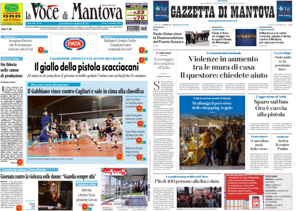 La foto mostra due pagine di giornale affiancate su uno schermo. A sinistra c'è "La Voce di Mantova" e a destra "Gazzetta di Mantova". Entrambi i giornali hanno articoli principali con titoli in evidenza. "La Voce di Mantova" ha un titolo che parla di una pistola scacciacani e una foto di una partita di pallavolo. La "Gazzetta di Mantova" ha un titolo che menziona l'aumento della violenza domestica e include una foto di un evento pubblico. Entrambi i giornali hanno vari articoli e immagini più piccoli distribuiti sulle loro pagine.  .