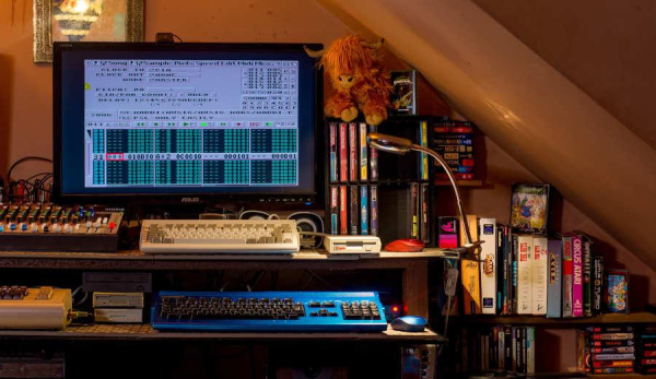 A vintage computer setup consisting of Amigas and a commodore 64. Amiga displaying on the screen with soundtracker pro II music editor on the screen. shelves of games with warm cosy lighting.