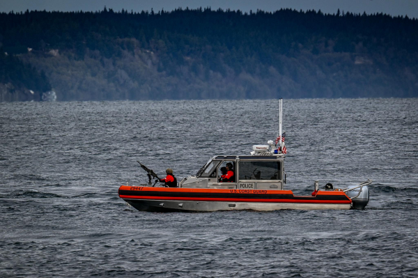 A small Coast Guard cutter with a machine gun mounted in the bow waits to escort a Washington State Ferry.