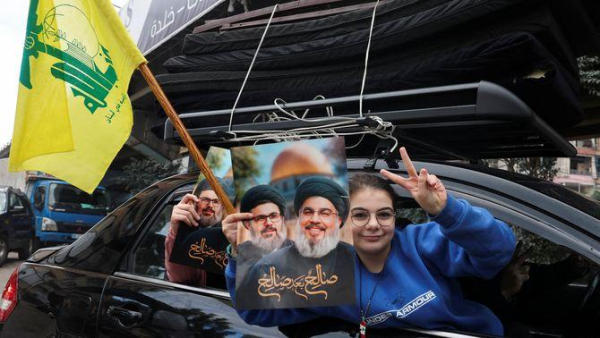 Una família amb matalassos al sostre del cotxe mostra una imatge de Nasrallah i Safieddine, líders de Hezbollah morts en atacs israelians (Reuters/Mohamed Azakir)