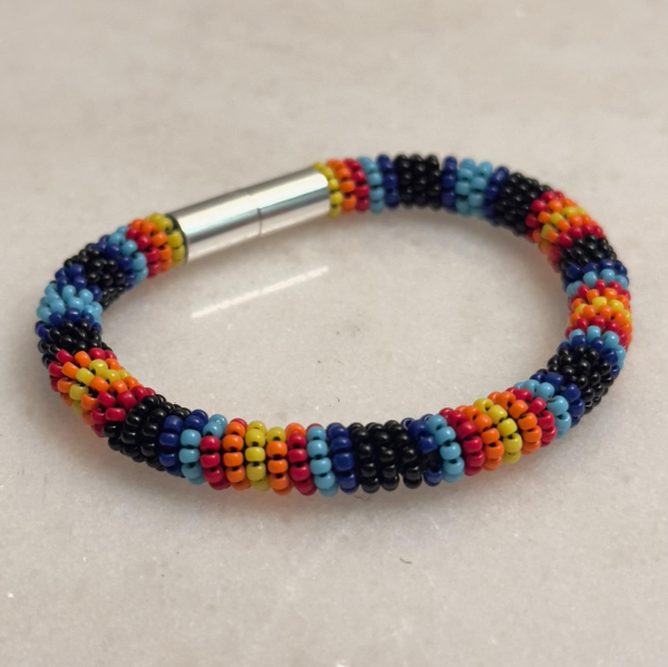 A black, blue, light blue, red, orange, and yellow bead-wrapped bracelet with a silver magnetic tube clasp on a marble background