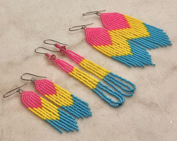 Three pairs of beaded earrings in the pansexual pride flag colors-- pink, yellow, and blue-- on a marble background