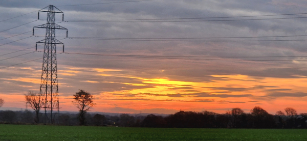 Sunrise over a field behind a pylon.