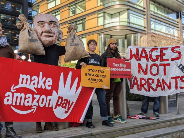 A group of people outside Amazon HQ. They have red and white signs and a paper sculpture of Jeff Bezos's head