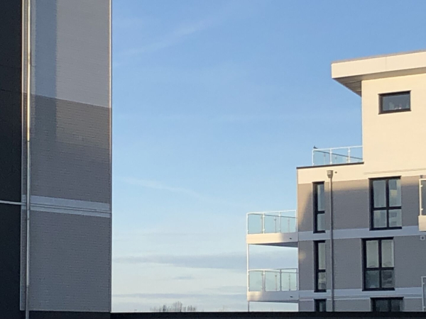 Zwischen weiß-grauen Häusern im Spalt ist hellblauer Himmel mit ähnlichen Farben wie in den Wasserbildern vorher. Links nur ein Stück Mauer, rechts Balkone und Fenster, eine versetzte Etage oben.