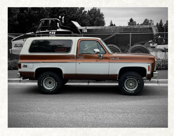 A GMC SIERRA sits in front of a construction zone, the car is red & white, the background is in black & white. 