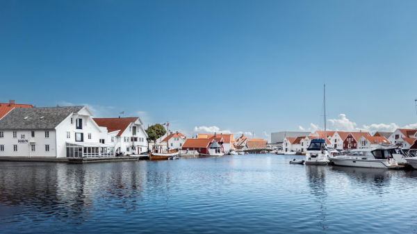 Widescreen view of boats and buildings in a small norwegian fishing village. Summer scene. Blue sky.