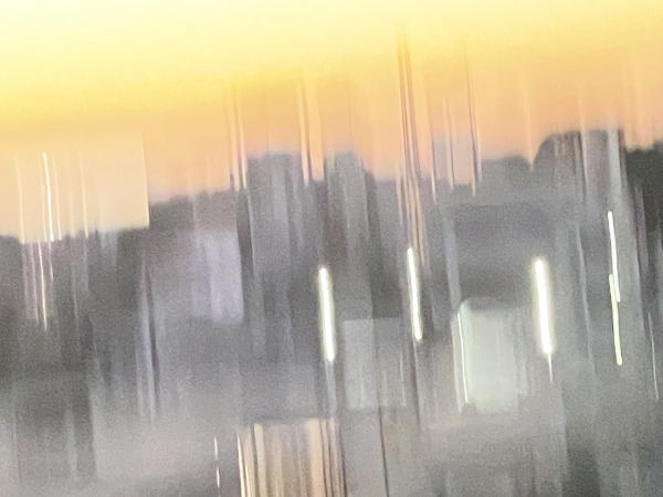 An abstract image featuring blurred silhouettes of buildings against a gradient sunset with soft orange and yellow hues.