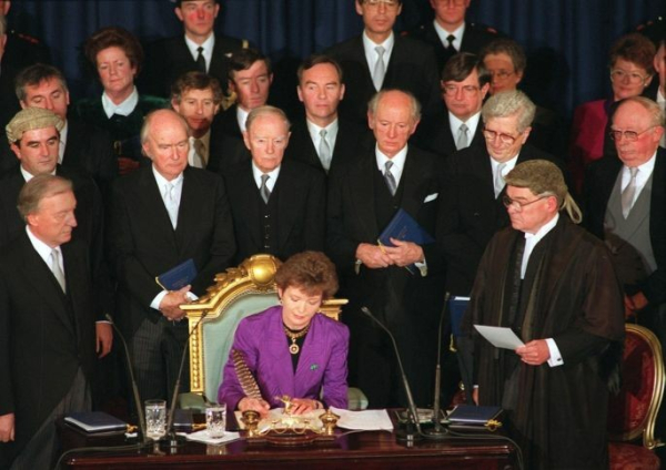 Mary Robinson signing the papers that made her President, with 17 men looking on. Everyone is white.