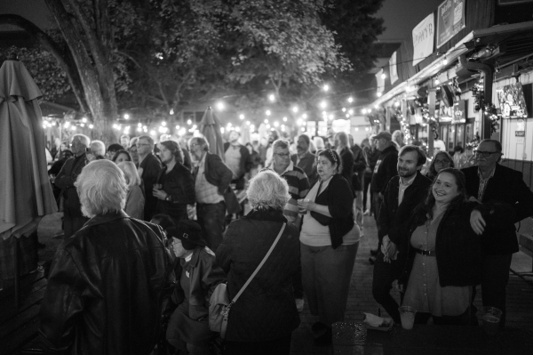 In black and white, a large crowd of current and former employees and many long time supporters of the Texas Observer celebrate in an outdoor courtyard under string lights.