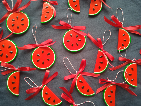 Many shiny watermelon decorations with red ribbons over a dark grey sheet.