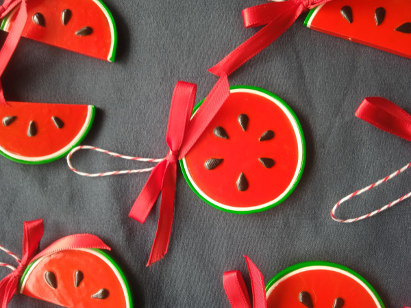 Close image of one of the watermelon decorations. A round polymer clay shiny watermelon with a red ribbon.