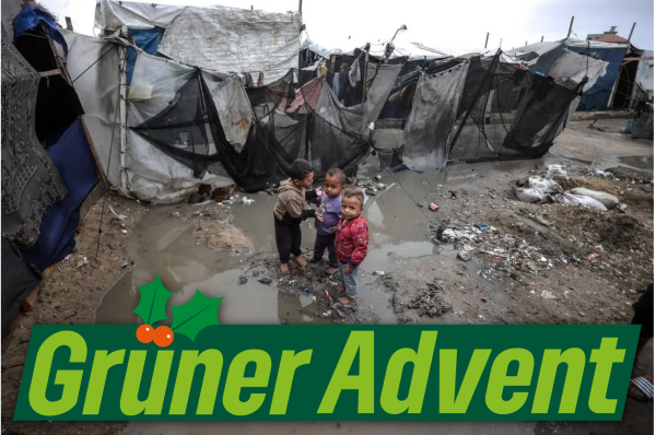 Im Hintergrund ein Bild des Lagers von Deir al-Balah in der Mitte von Gaza, Ende November, mit beschädigten Zelten, zwischen denen das Regenwasser steht. Auf dem Boden liegt Abfall. Auf einem kleinen Hügel im Wasser stehen barfüßig drei sehr kleine Kinder, zwei davon blicken in die Kamera. Im Vordergrund unten der Schriftzug "Grüner Advent", das ü ist weihnachtlich verziert mit Blättern und Beeren.