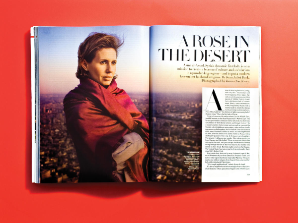 Two pages from Vogue magazine featuring an attractive photo of former Syrian first lady Asma Al-Assad, perhaps standing on top of a hill with a large city in the background. She is wrapped in a red shawl. The title of the article is "A Rose in the Desert".