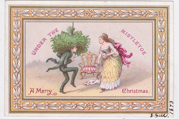 An illustrated Christmas card with a gold patterned border, "A Merry Christmas" in pink text across the bottom, and "under the mistletoe" arced over the top, also in pink. There is a person in a black suit crouched down under a huge mass of mistletoe. He is creeping towards a person in a pink and yellow frock with a large pink bow at the back, who is holding a fan and a posy of flowers. There is a gold, red and white throne like chair between and behind them both.