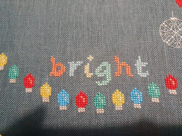 The word bright has been stitched above the fairy lights at the bottom of the pattern. The word is stitched in pale shades of red, blue, yellow and green. 