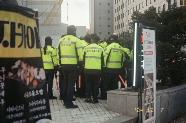 국회 근처 어느 골목 앞에 형광 점퍼를 입고 붉은 경광봉을 든 경찰들이 한데 모여 대기하고 있다.