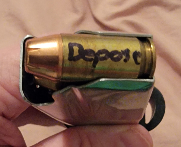 A pistol magazine filled with bullets and on the shell casing of the top bullet the word depose is written in black sharpie.