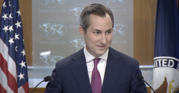 picture of a US politician speaking. There's a US flag and another flag with some North American seal. I judge his looks to be deceptive, like having no remorse to do whatever it takes to stay in power, or to gain more, be it his own or USA's, although I suspect his own is in a much higher priority.