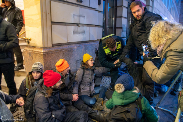 Aktivist*innen haben sich an den Händen miteinander verklebt. Polizisten prüfen, ob sie die Hände lösen können. Während der Blockade des Eingangs und der Tiefgarage des Hotels Adlon durch die Letzte Generation während des World LNG Summits. Berlin, 12.12.2024