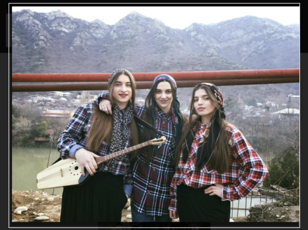 Trio Mandili pose in traditional Georgian dress with mandolin in front of a beautiful mountain range in Georgia