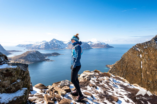 Enjoying the view. Woman in trailrunning clothes standing on a peak, a bit snow around. Mountains and the Atlantic Ocean in the background.