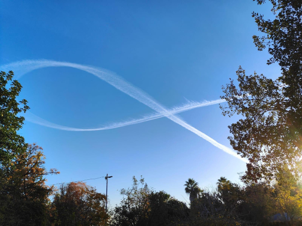 A contrail in the shape of a ribbon against a blue sky. 

The trail stats at one point, swings back on itself to create a loop and continues the other way. as if a scarf has been draped over an invisible neck. 

The trail starts and stopps at the same point crating a symetrical shape that looks allot like the reminder ribbon emoji. 