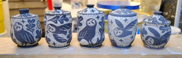 a line up of 5 lidded porcelain jars. they are all decorated with an owl design.