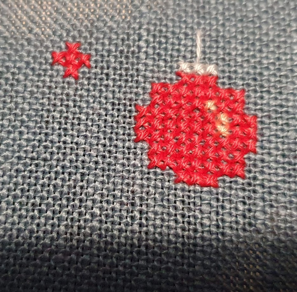 A little round red bauble. Cross stitched onto blue fabric. 