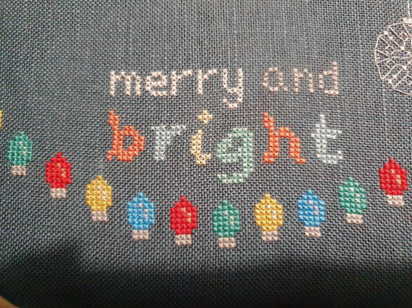 White and pale grey threads have added the words "merry and" to the ongoing cross stitch. 