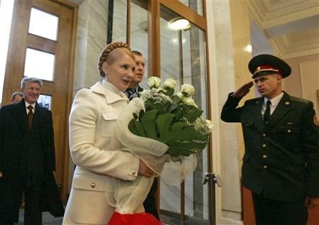 Yulia Tymoshenko walking into parliament as prime minster. She's a blonde white woman dress all in white, carrying flowers and being saluted by a guard.