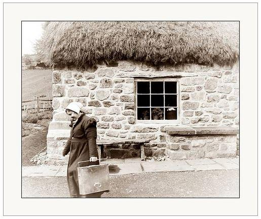 Vintage looking sepia photograph showing a domestic servant walking away from a thatched cottage.