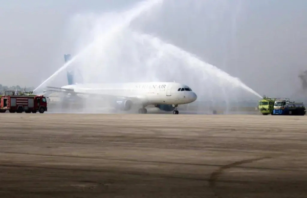 a plane on a runway being given a water salute by two airport firetrucks