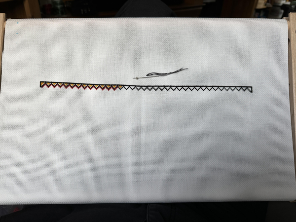 The beginning of a cross stitched border. Black zigzags under and solid black line. The zigzag is filled in with yellow and outlined in red