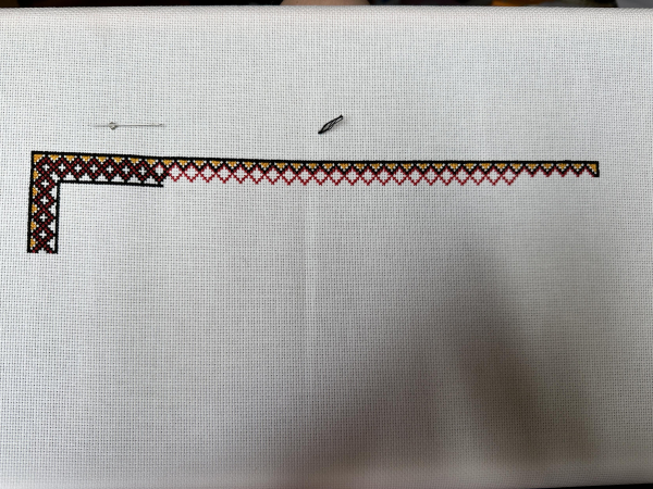 A decorative cross stitch border in black, red and yellow. 