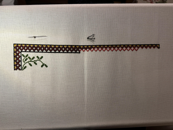 A partially completed cross stitch border in black, red and yellow. There are some small cross stitch leaves on the left inside the border 