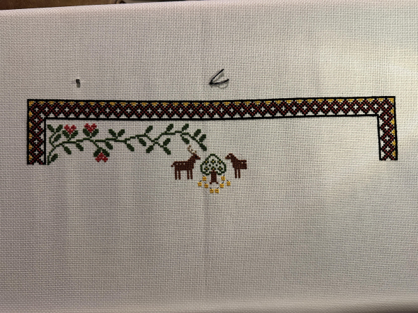 Partially completed cross stitch sampler. Border on the left, top and right is complete. Foliage and one and a half stags in the middle. 