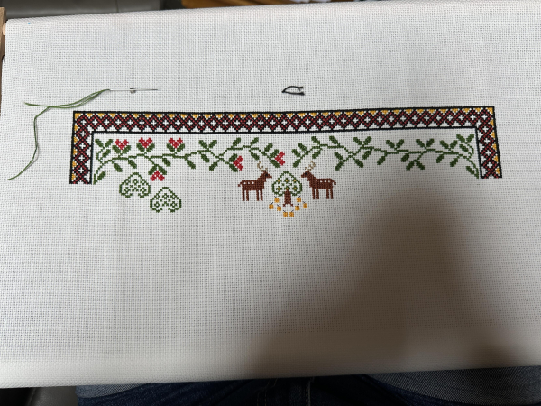 Partially completed cross stitch sampler border, leaves and stylised tree visible along with two tiny stags