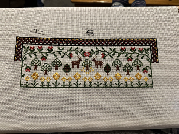 Top section of a cross stitch sampler.

Leaves, trees, deer and flowers visible. 