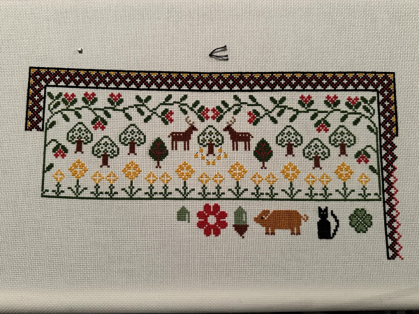 Cross stitch sampler. a red flower, acorn, orange pig, cat and a four leaf clover are at the bottom of it. 