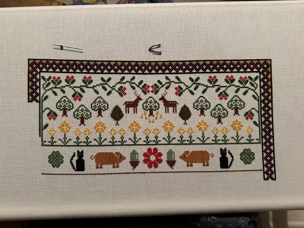 A WIP cross stitch sampler. The bottom section has from left to right a four leaf clover, a black cat, a Tamworth pig, an acorn, a red flower, an acorn, a Tamworth pig, a black cat and a four leaf clover. Symmetry in everything… 