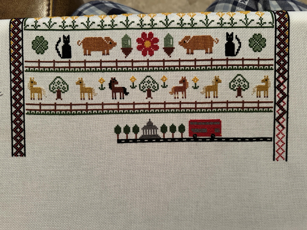 Cross stitch sampler. At the bottom is a London double decker bus on a road which hasn’t been finished yet