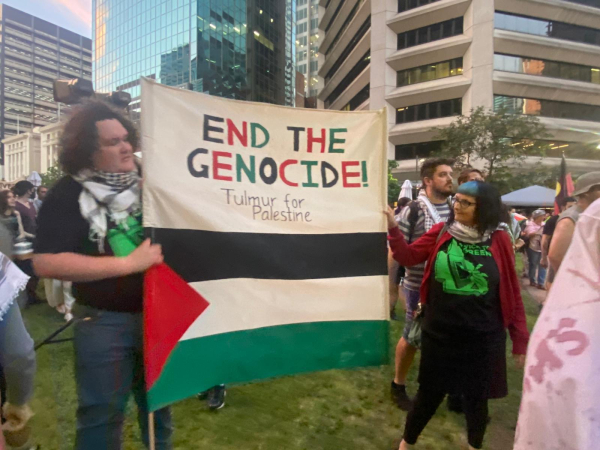 Two people wearing kuffiyeh hold a banner that reads: end the genocide, Tulmur for Palestine