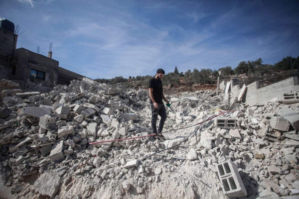 Photo; a man stands in the middle of rubble, captioned Palestinians inspect the destruction of a house after Israeli occupation forces carried out a demolition operation on the grounds of building without a permit in Nablus in the West Bank on November 14, 2024. Photo: Mohammed Nasser / Alamy