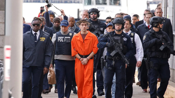 Luigi Mangione walks handcuffed and surrounded by police in an orange prisoner's outfit, wearing a crown of thorns. 