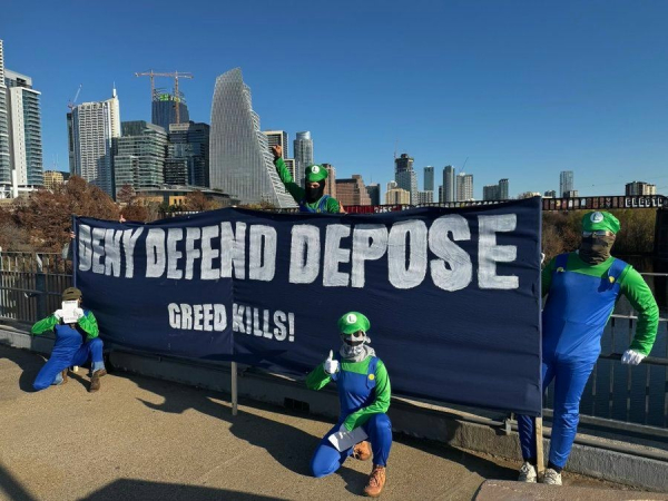 Group of people in Luigi costumes with banner reading, "Deny, Defend, Depose: Greed Kills!"